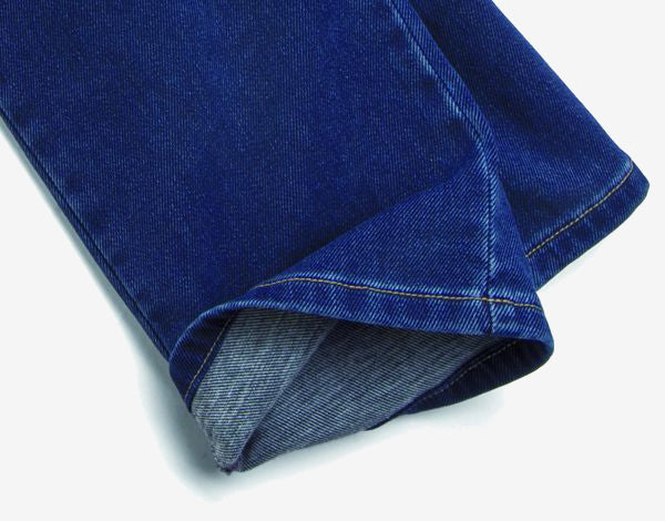 Eine Nahaufnahme eines gefalteten, dunklen blauen Jeanshosenbeins mit sichtbarer Naht, ausgestellt auf weißem Hintergrund.