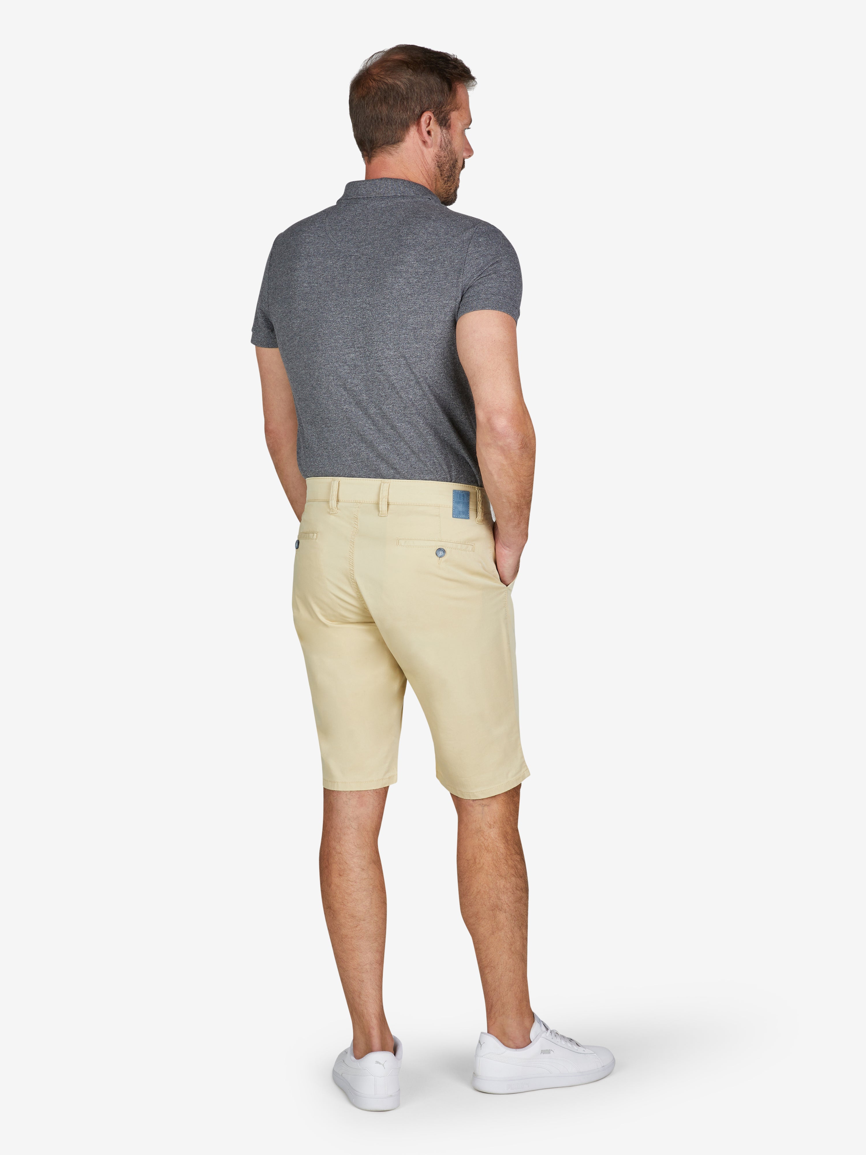 Männlicher Model trägt eine hellgelbe Bermuda-Hose mit regulärer Taille und Straight-Fit, kombiniert mit einem grauen Polo-Shirt. Die Shorts bestehen aus einem ultraleichten Baumwoll-Tencel®-Mix mit High Stretch, Komfortbund und Hemdenstopper, ideal für Frühling/Sommer.
