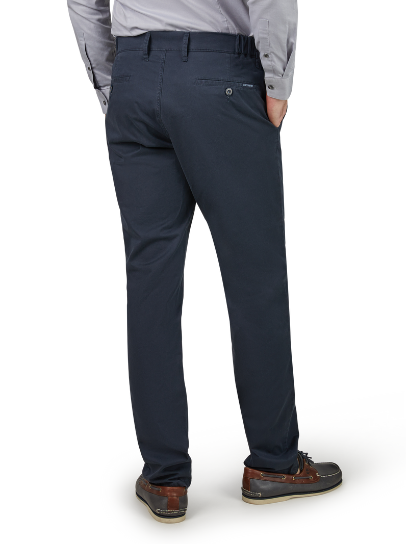 Ein Mann trägt schwarze Chino-Hosen, eine graue Hemd und braune Schuhe. Er steht mit den Händen in den Taschen, zeigt den Rücken zum Betrachter.