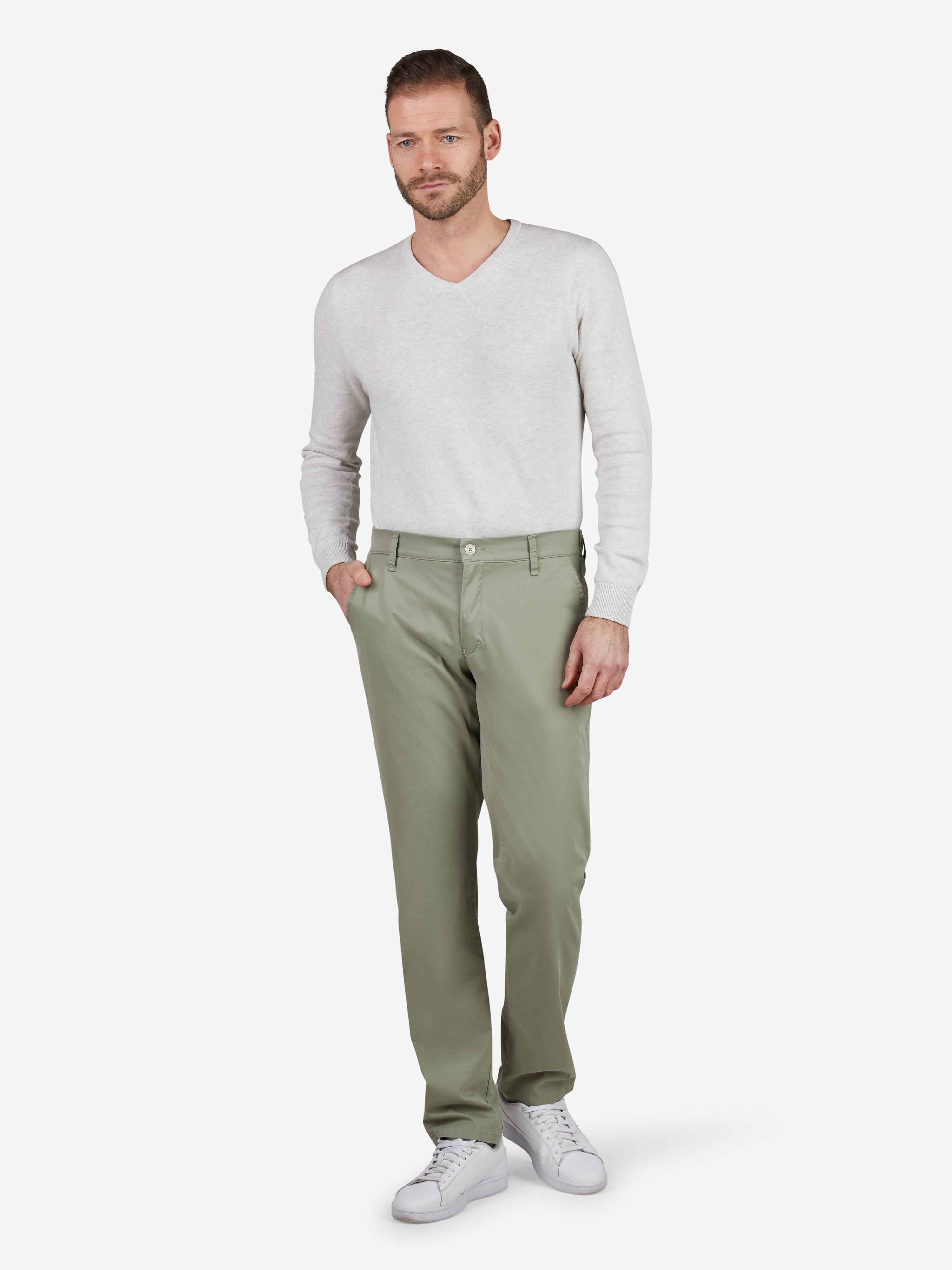 Mann trägt eine khakifarbene FOXX 8170 Hose aus sommerleicher Baumwolle mit Ultra-Flex-Bund, Hemdenstopper und Slim Fit bei schmaler Fußweite, kombiniert mit weißem Pullover und Sneakers.