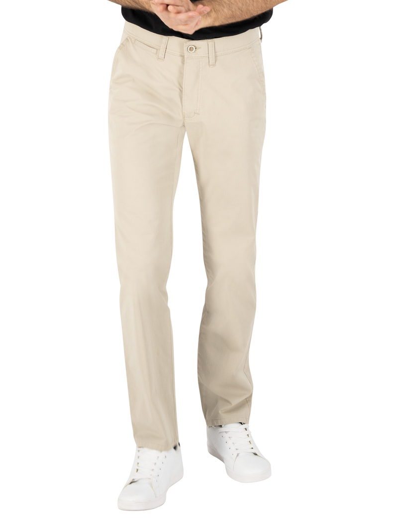 Ein Mann trägt beige Hose, die bis zu den Schuhen reicht, und weiße Sportschuhe. Er steht mit verschränkten Händen vor seinem Bauch.