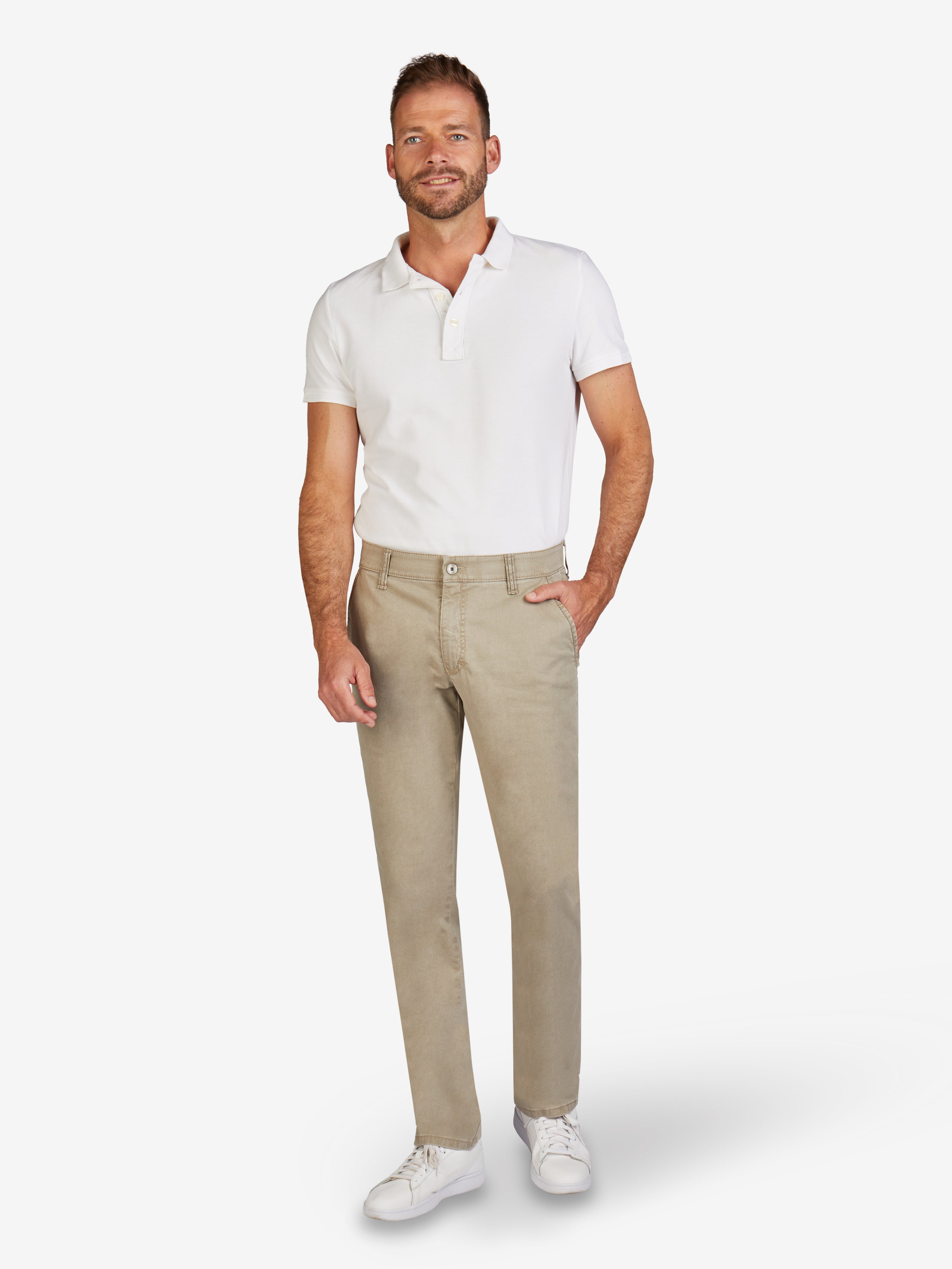 Mann trägt eine beigefarbene Flat Front-Hose mit elastischem Komfortbund, Hemdstopper und schmaler Fußweite, kombiniert mit weißem Polohemd und Sneakers, präsentiert das Produkt GARVEY 6701 grau-beige, eine komfortable Baumwoll-Broken Twill-Hose mit High Stretch, sportiven Kontrastdetails und sommerlichem Fade-Out-Färbeeffekt.