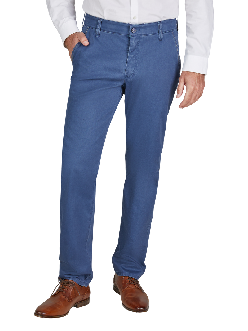 Mann trägt elegante, blaue Anzughose, die bis zu den Schuhen reicht, mit einer weißen Hemd. Seine rechte Hand steckt in der Hosentasche, die linke hängt locker an der Seite.