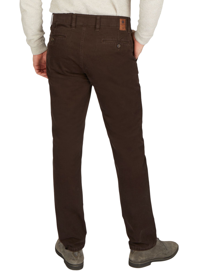 Der Bild zeigt eine Person, die braune Chino-Hosen trägt, die hinten zu sehen sind. Die Person trägt eine weiße, langärmlige Strickjacke, ihre Hände sind in den Taschen. Die Schuhe sind grau und robust.