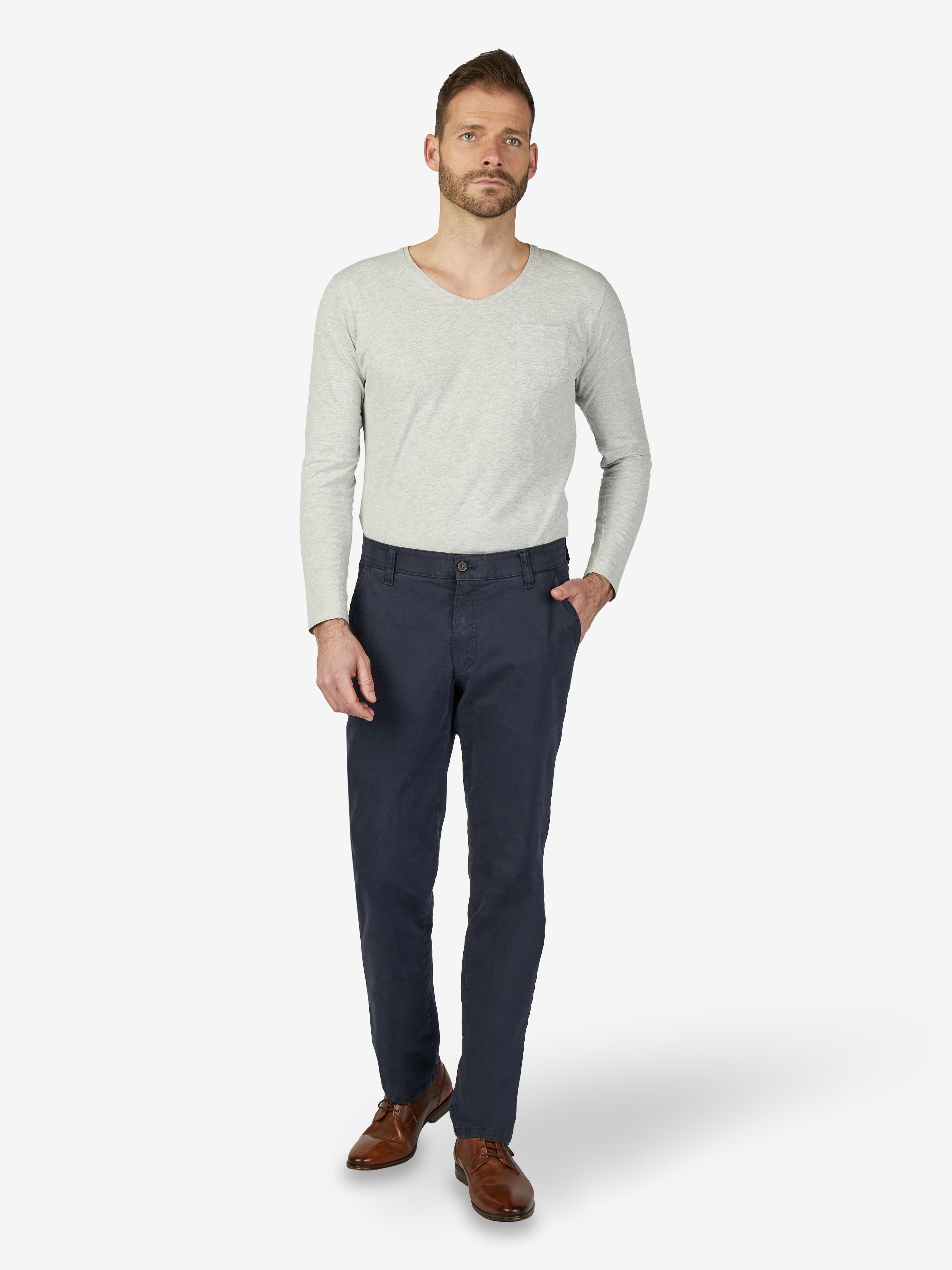 Mann trägt eine dunkelblaue GARVEY 7612 Flat Front-Hose mit Komfortbund, Hemdenstopper und Münztasche, kombiniert mit einem hellgrauen V-Ausschnitt-Pullover. Die Hose besteht aus hochelastischer Baumwolle, hat eine normale Leibhöhe, schmalen Beinverlauf und eignet sich für Herbst/Winter.