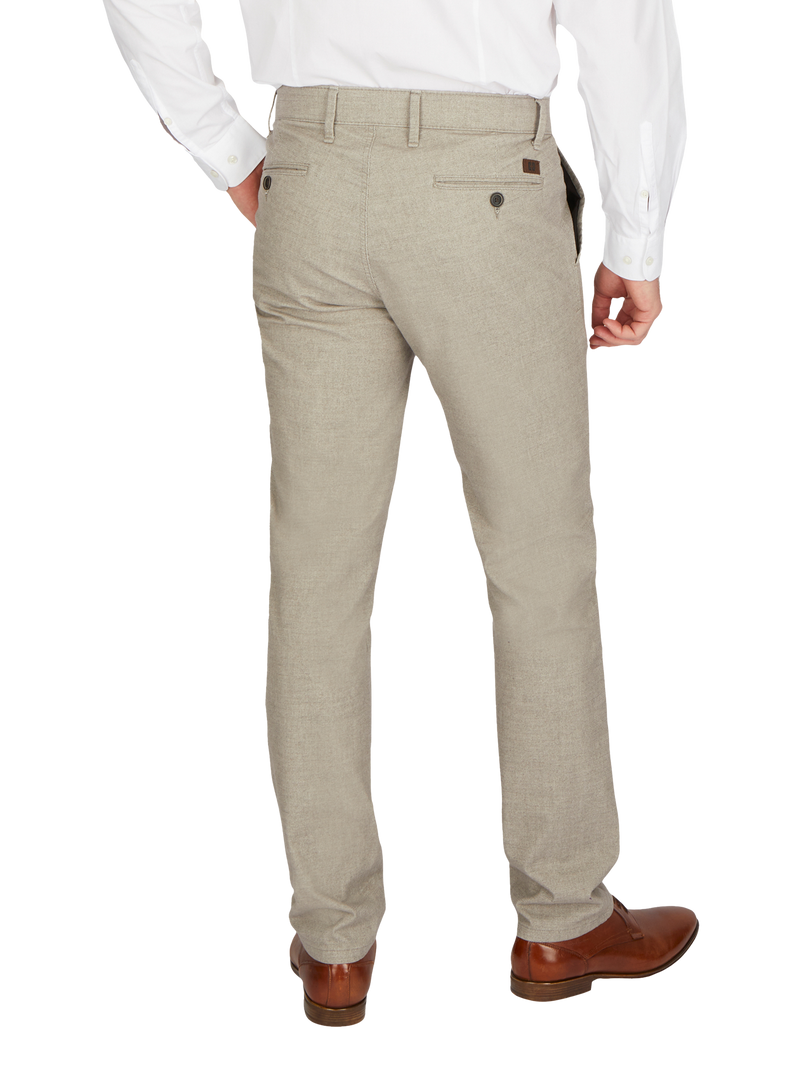 Mann in hellbeigen Anzughose, weißem Hemd, braunen Lederschuhen steht mit der Rückseite zur Kamera, eine Hand in der Hosentasche.