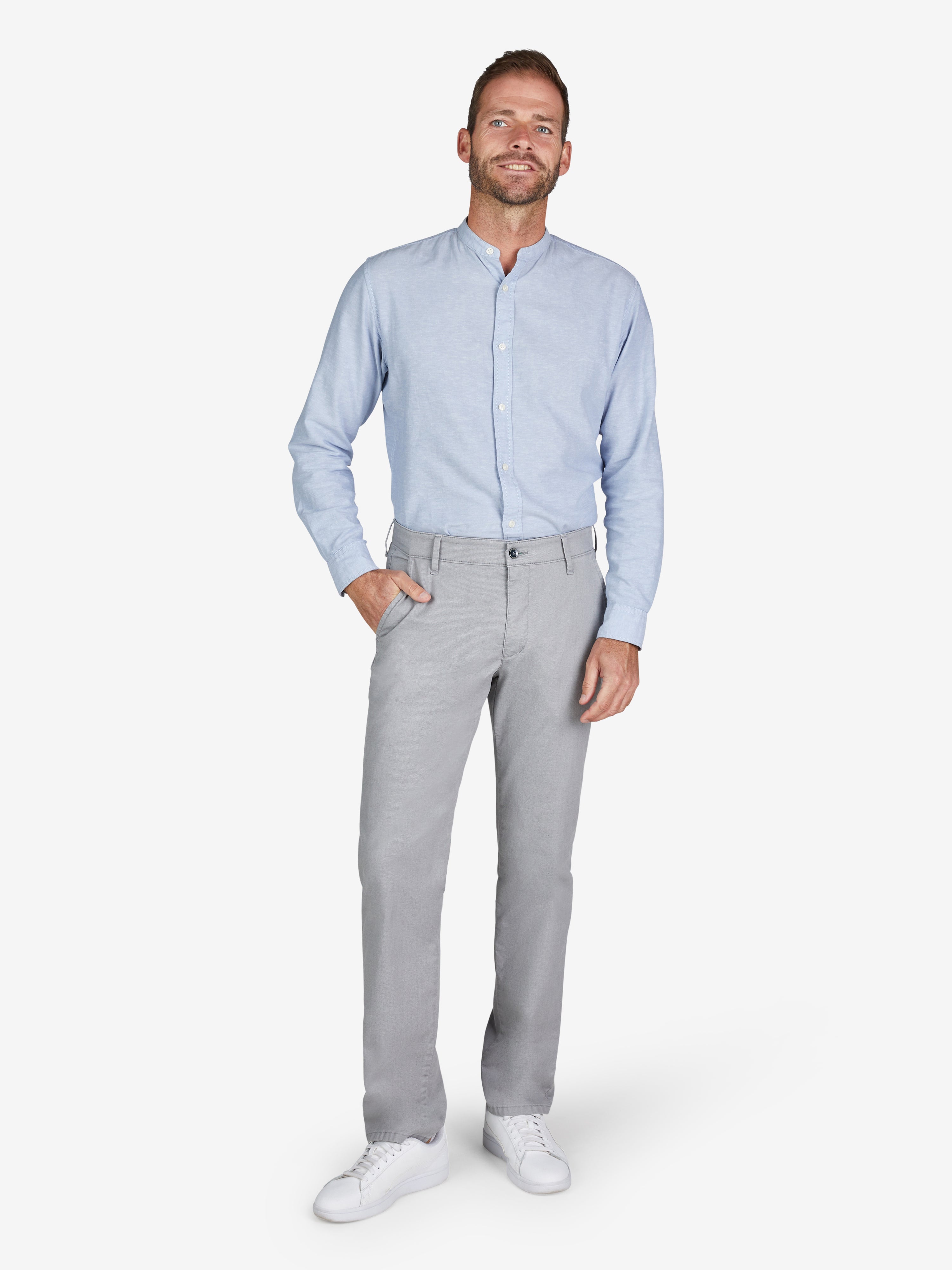 Mann trägt eine hellgraue GARVEY 8108 Flat Front-Hose mit elastischem Komfortbund und Hemdstopper, kombiniert mit einem hellblauen Hemd. Die Hose aus High Stretch Baumwoll-Mikrostruktur hat eine normale Leibhöhe, schmalere Fußweite und schlanken Beinverlauf, ideal für Frühjahr/Sommer.
