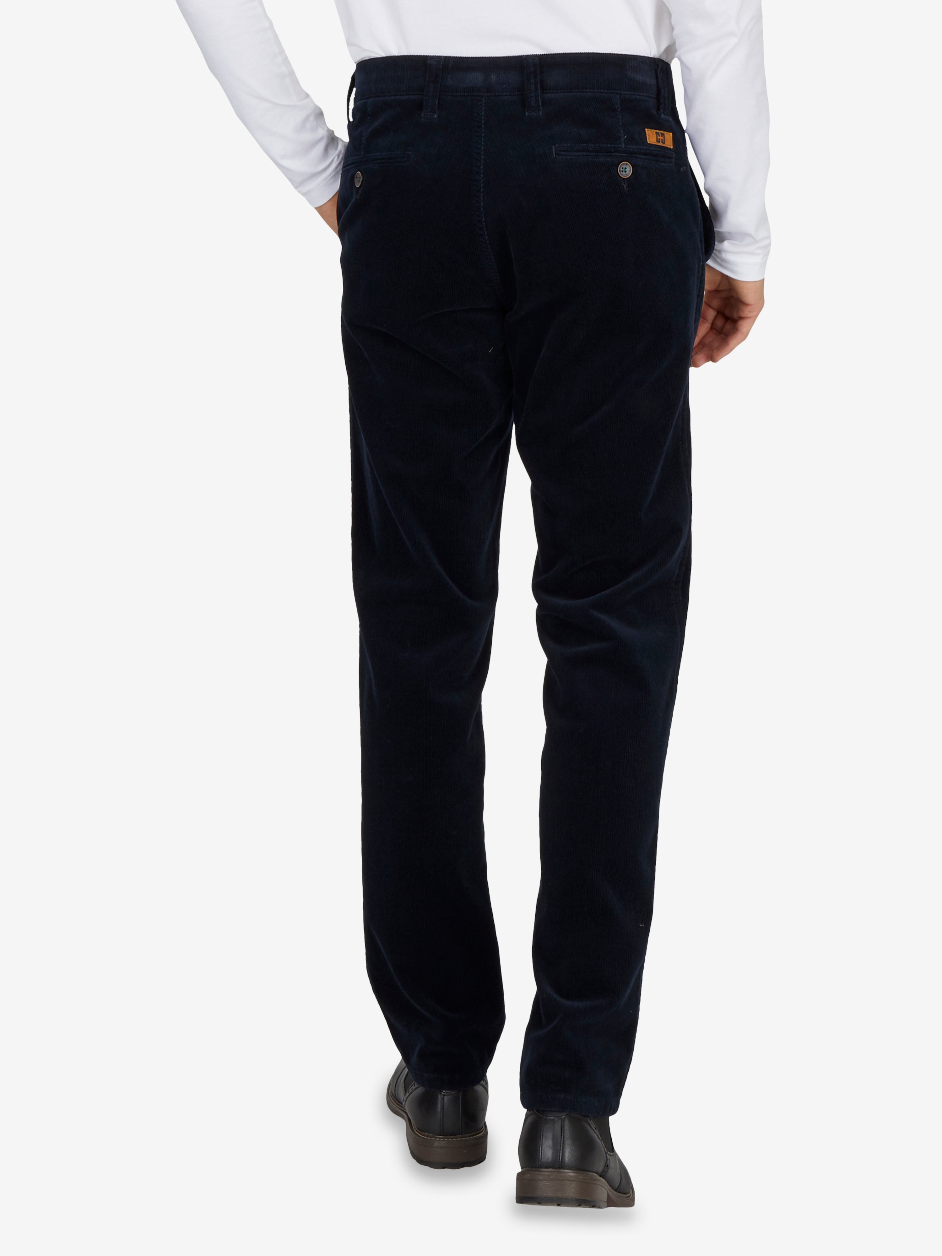 Nahaufnahme einer dunklen Flat Front-Hose aus Feincord mit High Stretch, elastischem Komfortbund, Hemdenstopper und Bundverlängerung mit Knopf und Haken. Das Modell trägt sie in normaler Leibhöhe, schlanker Beinverlauf, geeignet für Herbst/Winter.