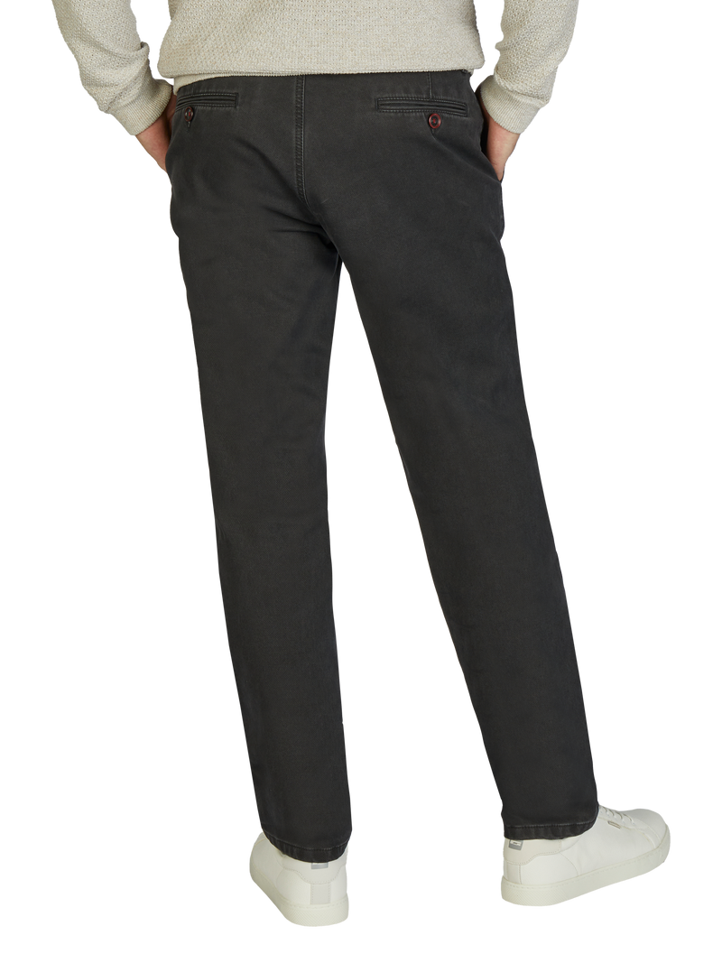 Ein Mann trägt dunkle Jeanshosen, die an die Hüften sitzen, mit den Händen in den Taschen, kombiniert mit weißen Sneakers und einem hellen Pullover, der nur teilweise sichtbar ist.