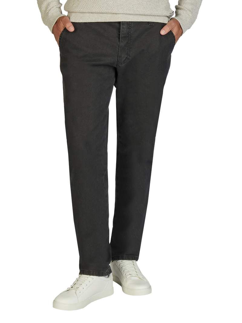 Nahaufnahme einer Person, die dunkle Jeans trägt, mit Händen in den Taschen, kombiniert mit weißen Sneakers und einem hellen Pullover. Der Fokus liegt auf den Hosen, die leicht lockergelassen sind.