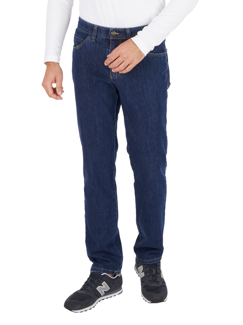 Ein Mann trägt dunkle Jeans, ein weißes Langarmshirt und schwarze Sportschuhe. Die Person steht mit einer Hand in der Tasche und ist nur von den Schultern abwärts bis zu den Füßen sichtbar.