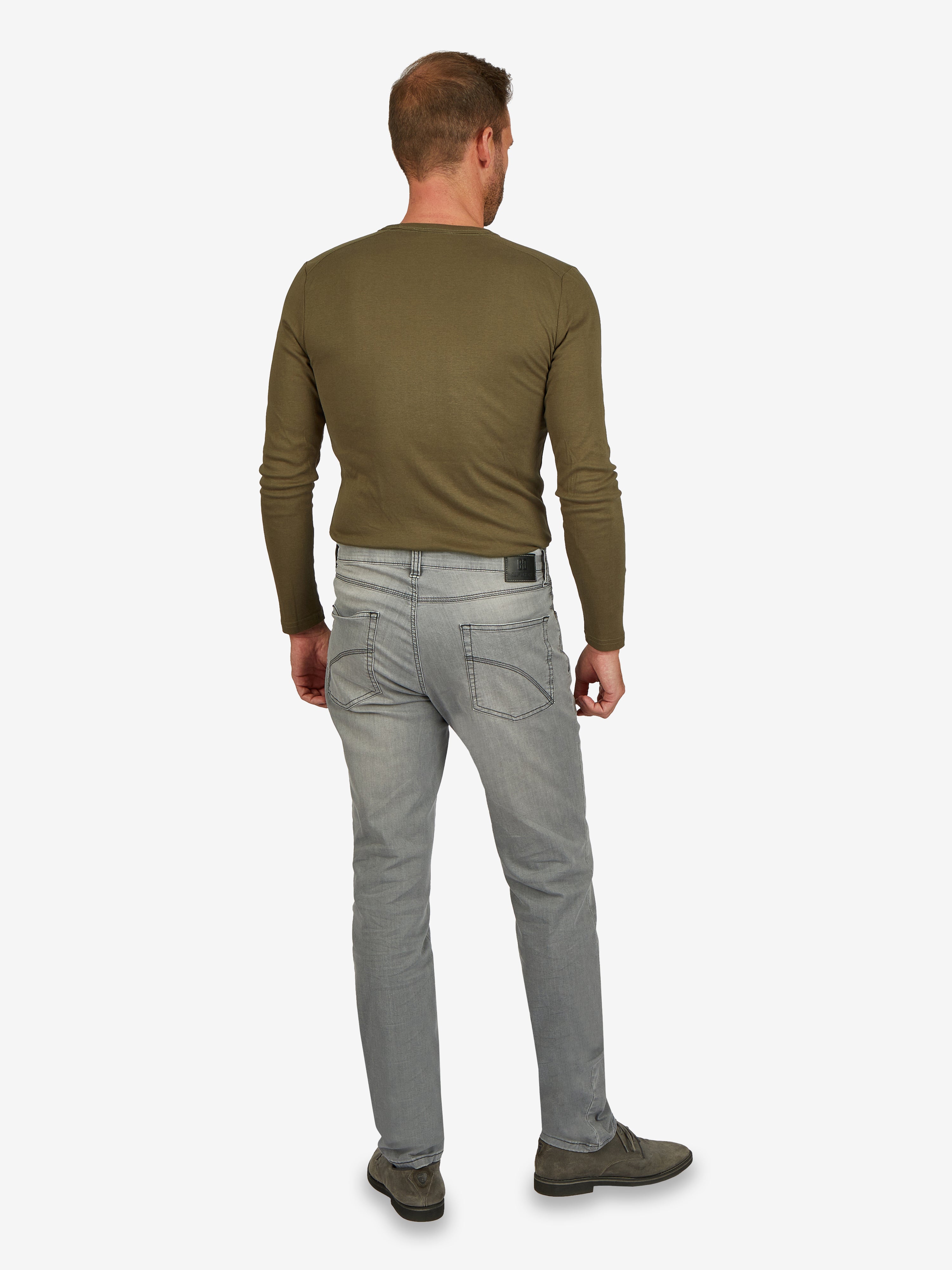Mann trägt eine hellgraue, elastische 6-Pocket Jeanshose von Club of Comfort, Modell HENRY 6516, mit normaler Leibhöhe, schmalem Bein, Mobile Pocket, Münztasche mit Kontrast-Patch, aus Super High Stretch-Denim, in einem hellgrauen, gewaschenen Look.