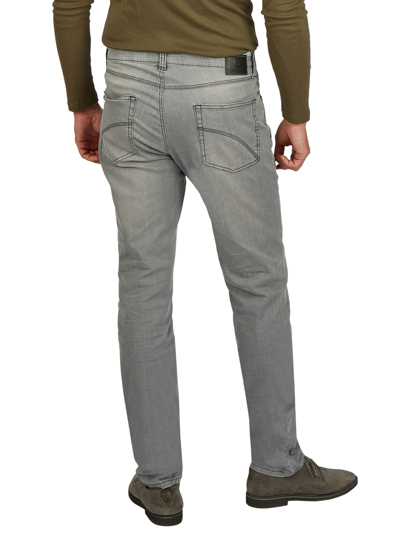 Ein Mann steht mit seinem Rücken zur Kamera, trägt eine graue Jeans, eine braune Langarmjacke und braune Schuhe.