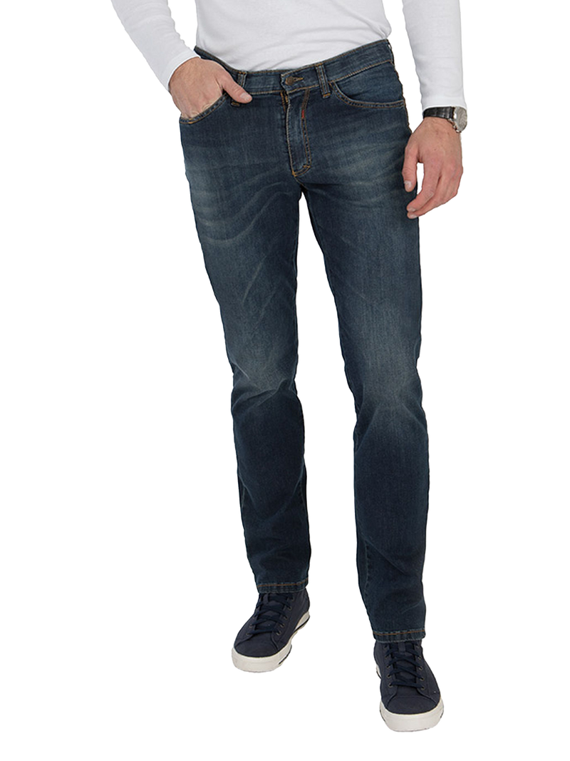 Ein Mann trägt dunkle Jeans, die leicht abgenutzt aussehen, mit einer weißen Langarm-Shirts. Er hat eine schwarze Armbanduhr an seinem rechten Handgelenk, seine linke Hand steckt in der vorderen Tasche. Er trägt schwarze Sneakers und steht mit leicht angewinkelten Beinen.