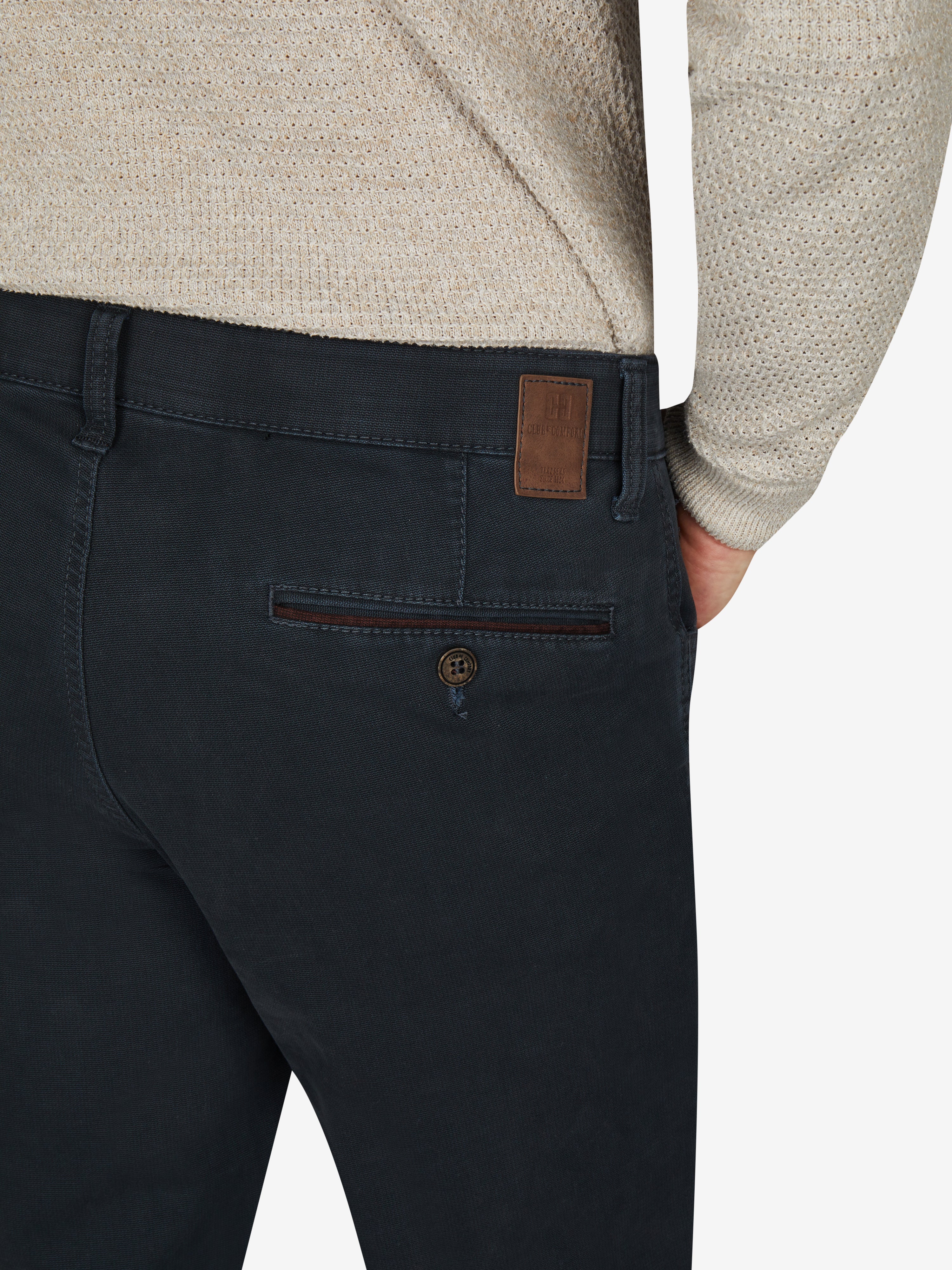 Nahaufnahme einer dunkelblauen MARVIN 7218 Hose mit elastischem Comfortbund, Hemdenstopper, Doppel-Paspelierte Münztasche, hergestellt aus Mikrostruktur-Baumwolle mit High Stretch, modifizierte 5-Pocket-Form, hergestellt von Club of Comfort, für Herbst/Winter, mit braunem Labels, seitlicher Ansicht.