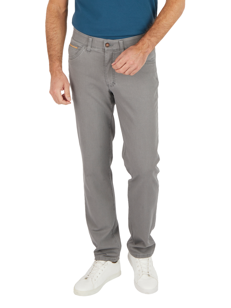 Mann trägt helgraue Jeans, blaue T-Shirt und weiße Sneakers. Das Bild zeigt den oberen Körper bis zu den Füßen, wobei er eine Hand in die Hosentasche steckt.