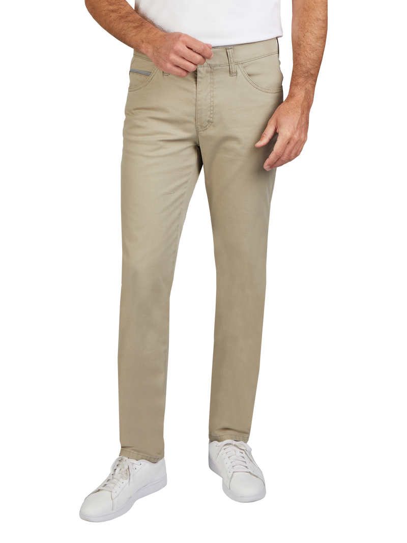 Mann trägt beige Jeans, weißen T-Shirt und weiße Sneakers. Der Fokus liegt auf den leicht ausgestellt, geraden Jeans, die bequem aussehen.