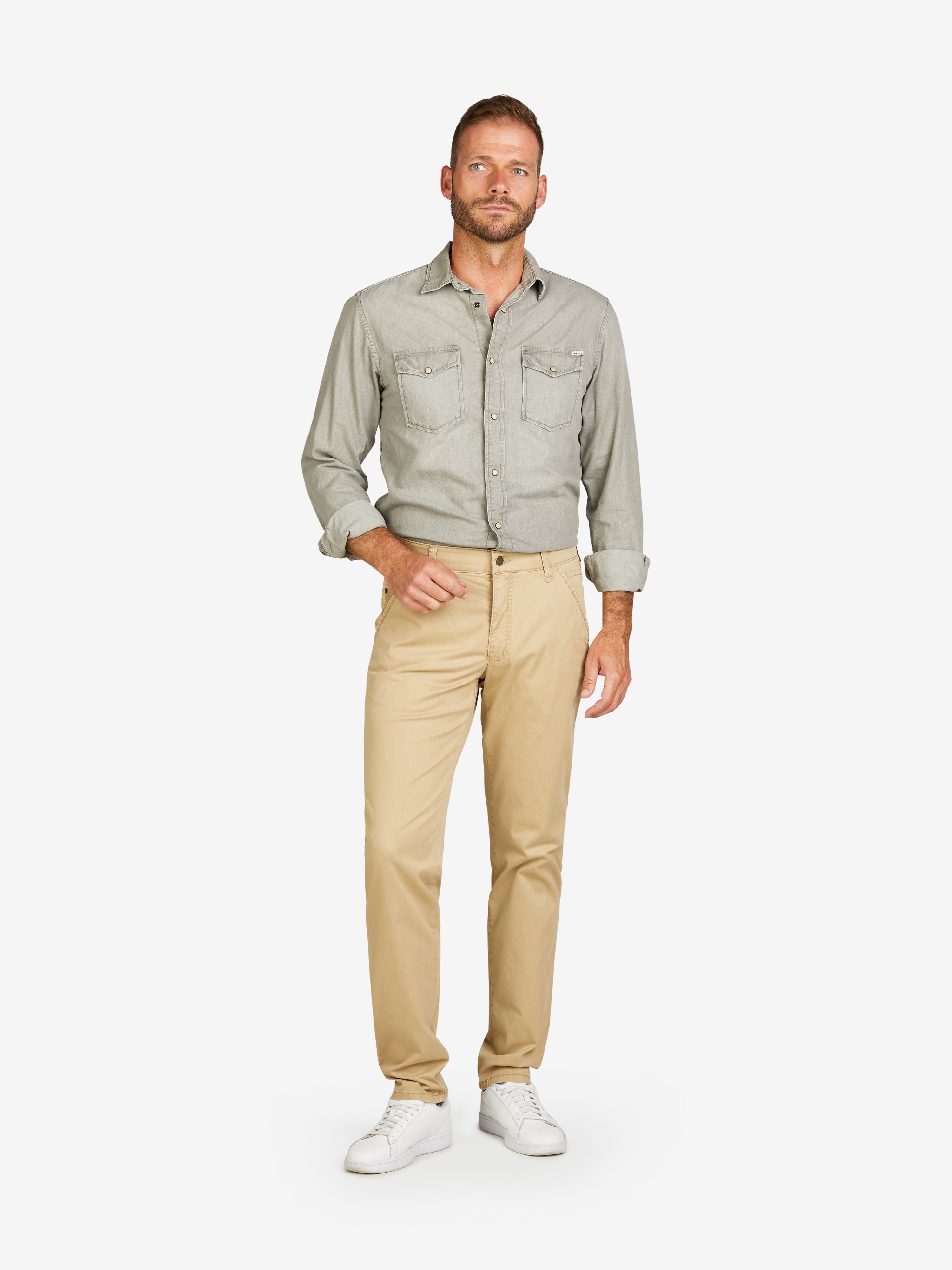 Mann trägt eine beige Chino-Hose von Club of Comfort mit Slim Fit, elastischem Comfortbund, Hemdstopper und Münztasche, aus leichtem Baumwoll-High Stretch, normale Leibhöhe, extra schmaler Beinverlauf, Modell PHIL 7708, Frühjahr/Sommer.
