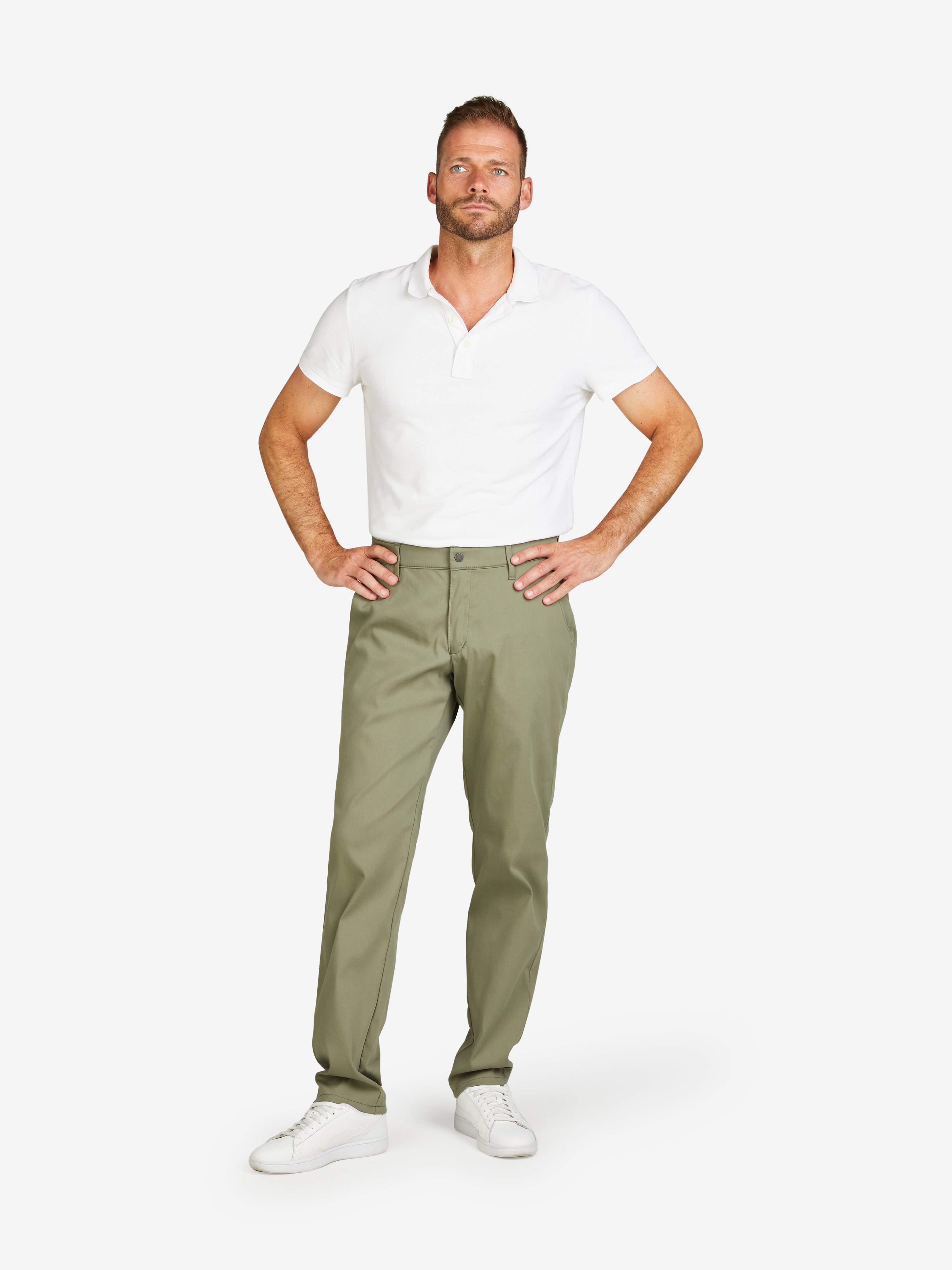 Mann trägt grüne ROB 8130 Chino im Tapered Fit mit elastischem Comfortbund, Hemdenstopper und High Stretch Baumwollqualität, Kombination mit weißem Polo-Shirt, neutrale langweiße Hintergrund.