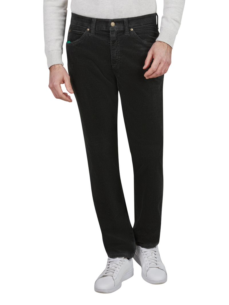 Hüftlange schwarze Jeanshose an einer Person, die eine graue Langarmjacke trägt und weiße Turnschuhe anhat. Die Person steht aufrecht mit einer Hand an der Seite und der anderen Hand an der Hüfte.