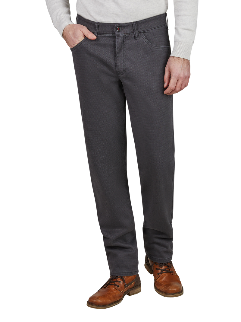 Die Abbildung zeigt eine Person in dunklen Jeans, die mit der linken Hand in die Tasche greift. Die Person trägt braune Lederschuhe und ein hellgraues Oberteil.