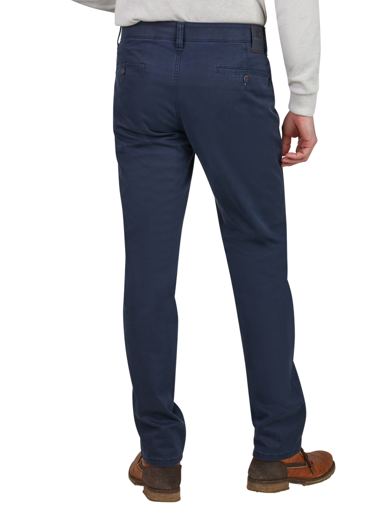 Blick auf die Rückseite eines Mannes, der dunkelblaue Chino-Hosen trägt. Er steht mit leicht angewinkeltem Bein, trägt braune Schuhe und ein graues Oberteil. Die Hosen haben angeschnittene Gesäßtaschen und eine schlanke Passform.