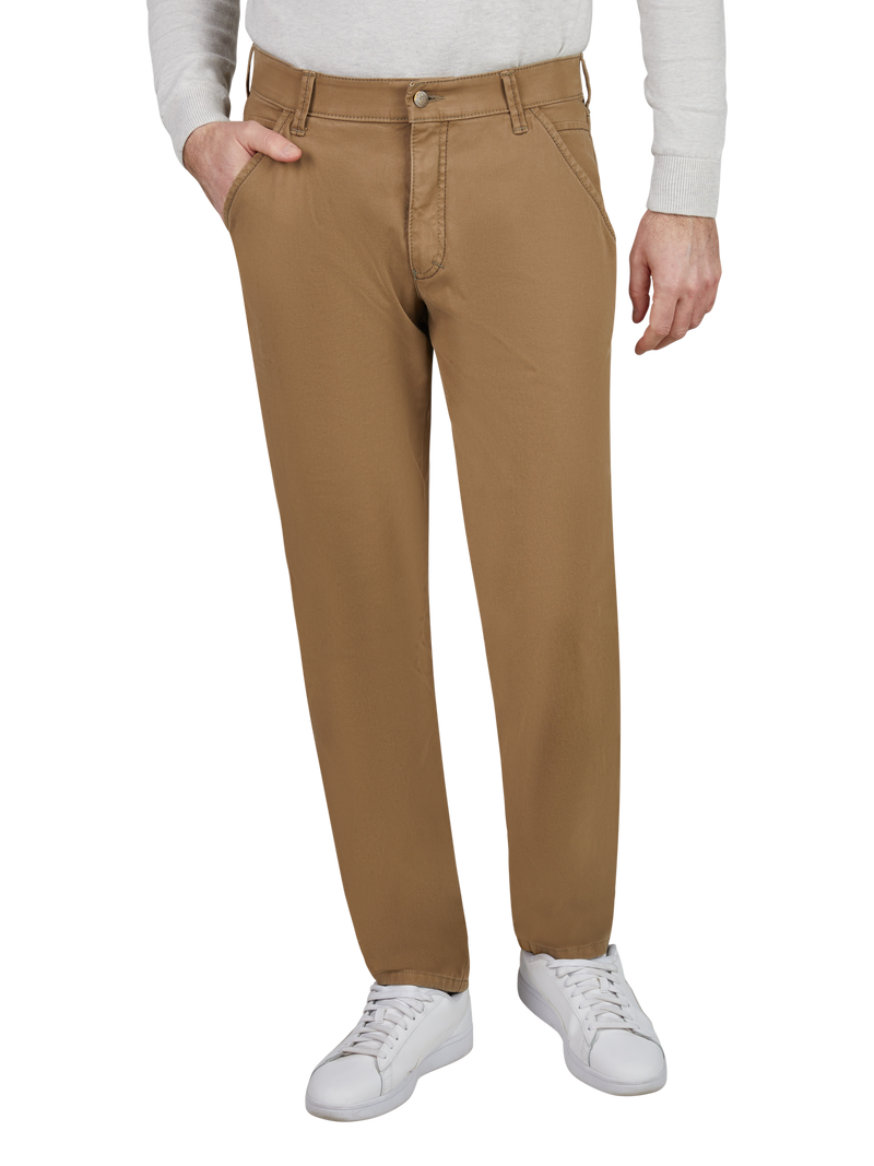 Nahaufnahme einer Person, die eine beige Hose trägt. Die Hose hat eine normale Passform, Gürtelschlaufen, Seitentaschen und einen Knopfverschluss. Die Person trägt eine helle lange Ärmel-Top und weiße Sportschuhe.