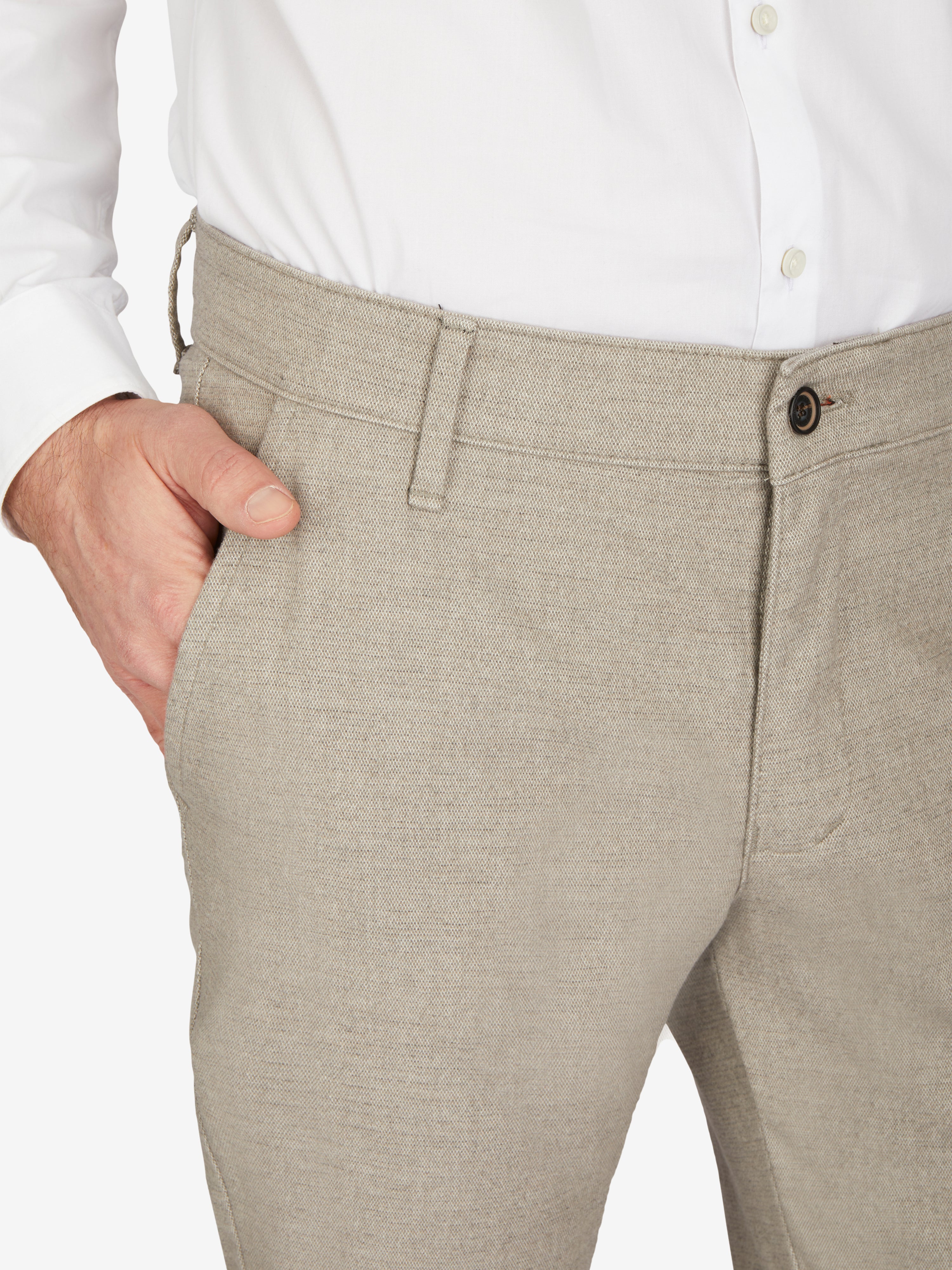 Nahaufnahme einer hellgrauen, melierten Flat Front-Hose "GARVEY 7631" in Regular Fit mit elastischem Komfortbund und Hemdstopper, gefertigt aus Baumwoll-Struktur-Mischgewebe mit Wool-Look, für Herbst/Winter, modeliert an einer Person in weißem Hemd.