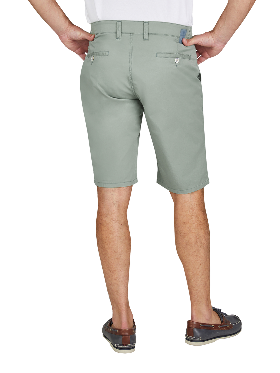 Blick auf die Rückseite eines Mannes, der eine hellgrüne kurze Hose trägt. Die Hose hat zwei Gesäßtaschen mit Knöpfen und Gürtelschlaufen. Der Mann steht mit den Händen in den Hüfttaschen, trägt braune Schuhe und ein weißes Oberteil.